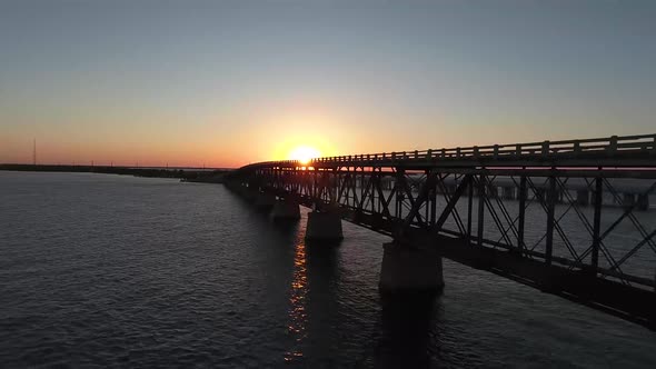 AERIAL: Pull back and rise up over an old bridge in the middle of the ocean at sunset. alt