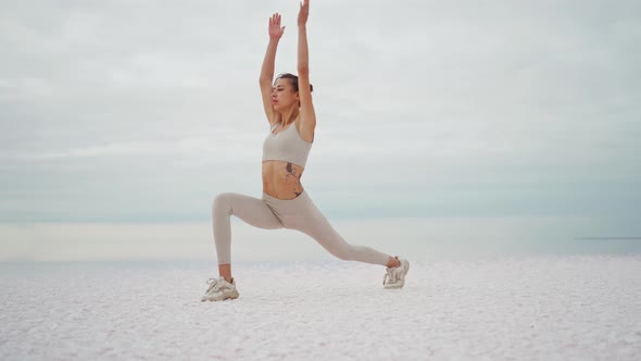 Young Woman Training in Nature on the Beach in Front of Dry Lake and Cloudy Sky alt