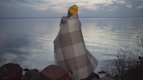 Wide Shot of Charming Young Caucasian Woman in Yellow Hat Wrapping in Blanket and Turning To Camera alt