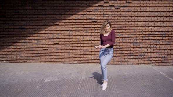 Pretty Woman Counts and Dances Near Red Brick Wall on Street