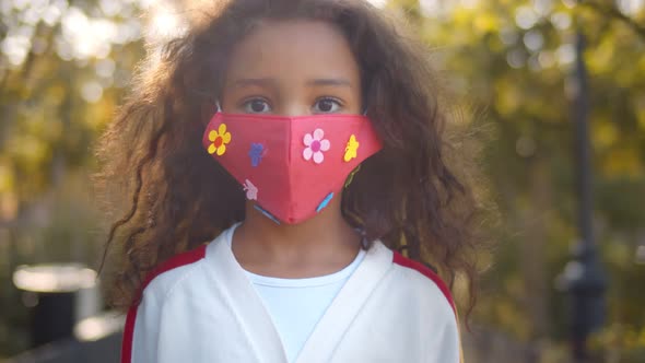 Portrait of Small African Girl with Face Mask Standing Outdoors alt