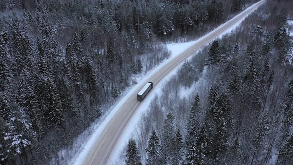 A Truck is Driving on the Road Through the Winter Forest alt