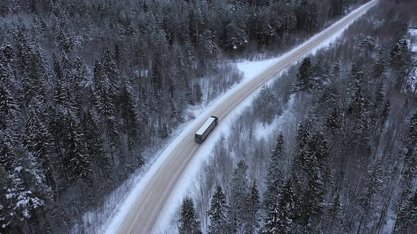 A Truck is Driving on the Road Through the Winter Forest