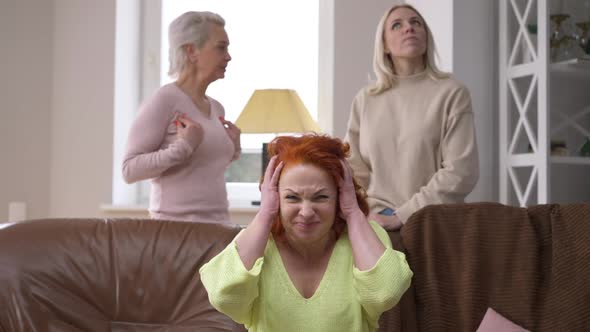 Portrait of Sad Worried Redhead Woman Closing Ears with Hands As Friends Arguing at Background alt