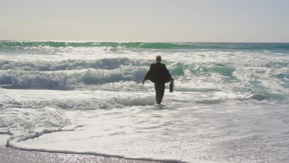 Businessman walking towards sea on beach in the sunshine 4k