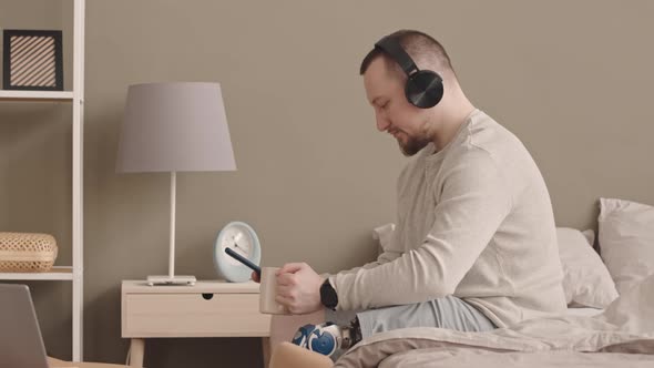 Man with Prosthetic Leg Listening to Music in Headphones at Home alt