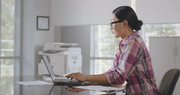 Side View of Asian Businesswoman Working on Laptop Sitting at Desk in Modern Office alt