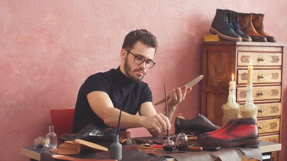 Young Designer Using a Brush While Working in Shoe Shop with Modern Interior