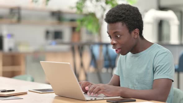 Excited Young African Man Celebrating Success on Laptop alt