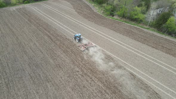 Farmer preparing soil in the farm field with perfectly straight rows. Clouds of dusty dirt billowing