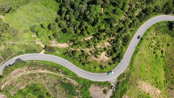 Aerial view of the road against the backdrop of green mountains along which the car is traveling.