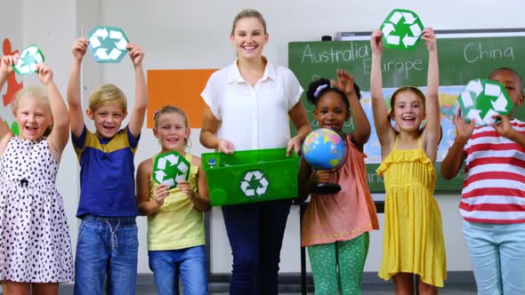 School kids and teacher holding recycling symbols and globe in classroom alt