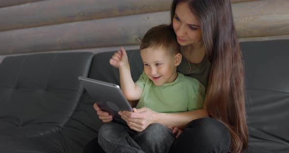 Young Smiling Mother and Her Sweet Son Playing in a Child Development App on a Digital Pill in a alt