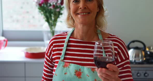 Portrait of smiling woman showing a glass of red wine in kitchen alt
