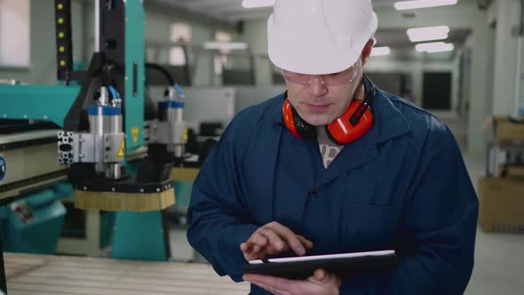 A Male Factory Worker Uses a Tablet in the Workshop alt
