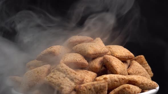 Hot crispy chocolate pads rotation with smoke in macro on black background. Cereal dessert alt