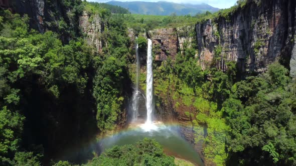 Drone shot of Mac Mac Fall in South Africa - drone is reversing from the waterfall, showing a rainbo alt