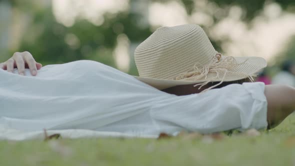 Asian woman while lying on the field green grass and have fedora hut closes her face.