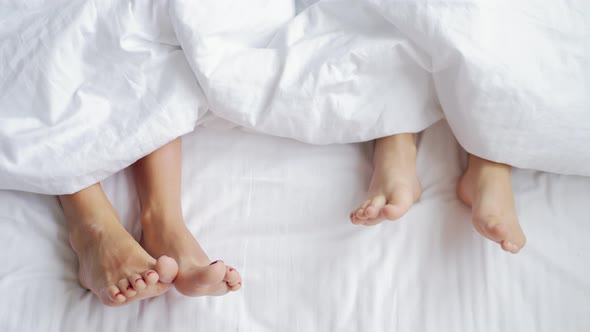 Mother and Child Lie on Bed with White Sheets Feet Side By Side in Comfortable Bed at Home alt