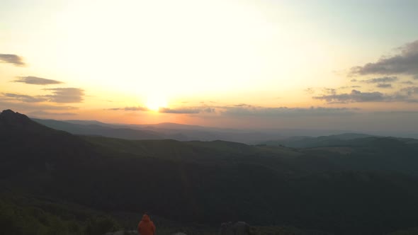 Mountain Hiker with Map Taking Rest at Sunset Sitting on Mountain Peak and Enjoying the Sunset alt