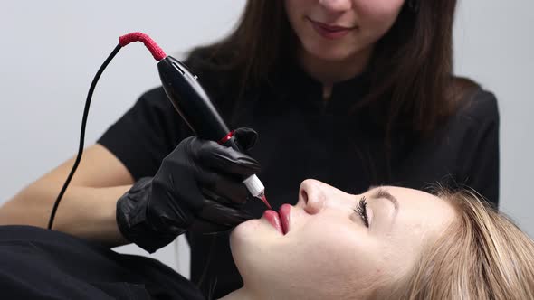 Cosmetologist Applying Pink Pigment Permanent Tattoo on Female Lips with Tatooing Needle Machine