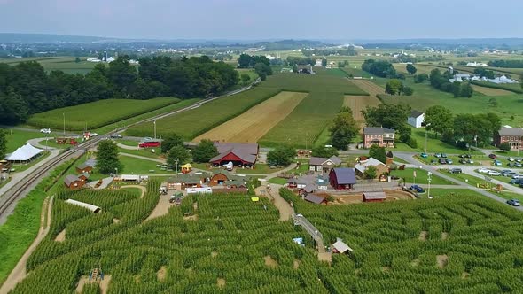 Aerial Rising View of a Corn Maze and Fertile Farmlands with a Railroad Track alt