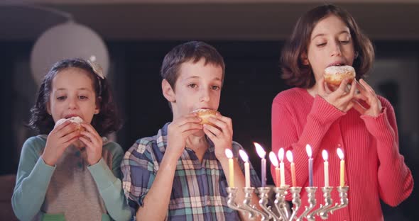 Kids and their mother eating donuts with a menora and dreidels alt