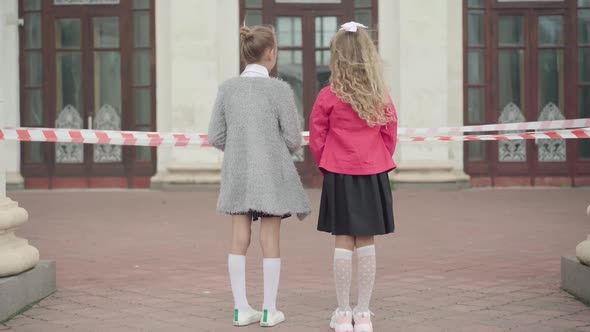 Wide Shot of Two Girls Standing in Front of Closed School During Coronavirus Lockdown. Sad alt