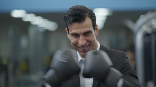 Closeup Portrait of Smiling Happy Confident Man in Formal Suit and Boxing Gloves Posing in Gym alt