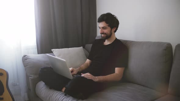 Happy Man Relaxing on Couch While Video Calling Using Laptop at Home alt