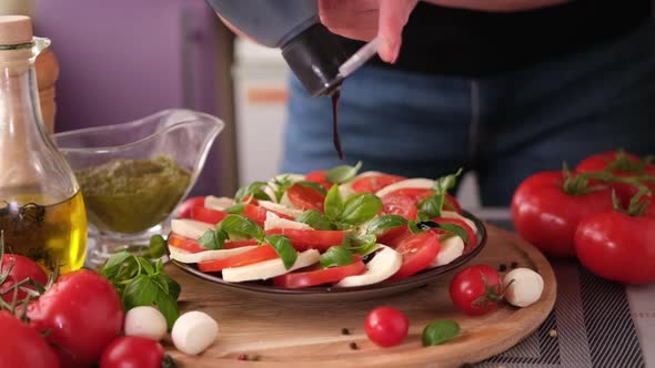 Pouring Balsamic Sauce on Caprese Salad with Cherry Tomatoes and Mozzarella Cheese Balls alt