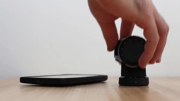 Man Puts a Smartphone on the Bamboo Table and a Smartwatches on the Charging Dock Station alt