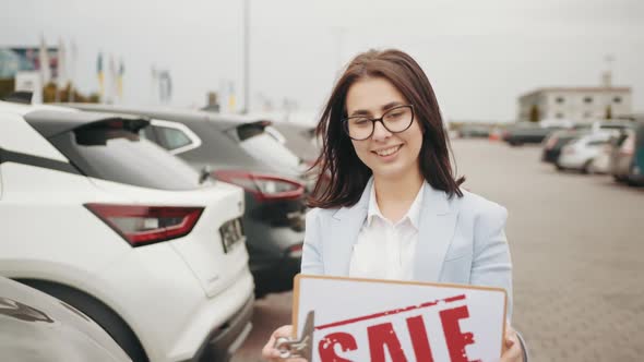 Smiling Caucasian Woman with Dark Hair Holding Sale Banner in Hands While alt