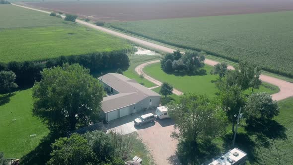 Drone aerial view of a sprawling home, farm yard, standing water, corn fields and a gravel road in r alt
