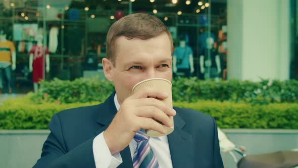 Handsome Caucasian Middle Aged Businessman Stands in the Street with Great Views and Drinks Hot alt