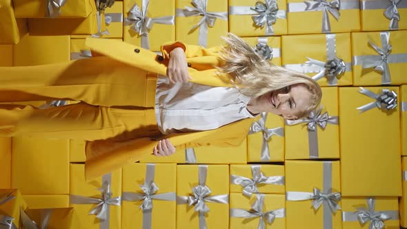 An Attractive Blonde in a Yellow Suit Poses Against the Background of Yellow Gift Boxes