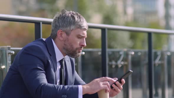 Businessman drinking coffee and using smartphone outside