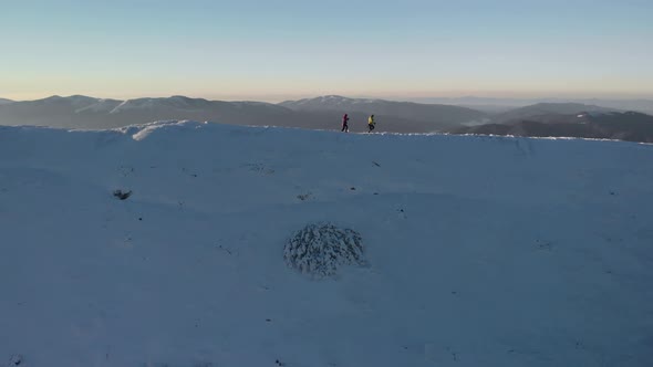 Drone Following Young Couple of Hikers, Walking on Mountain Ridge in Winter