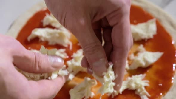 baker prepares traditional Italian pizza. cook puts pieces of cheese on dough.