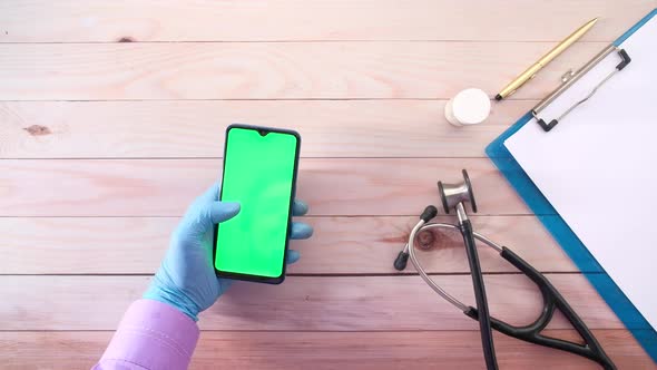 Top View of Hand in Latex Gloves Holding Smart Phone on Clinic Table alt