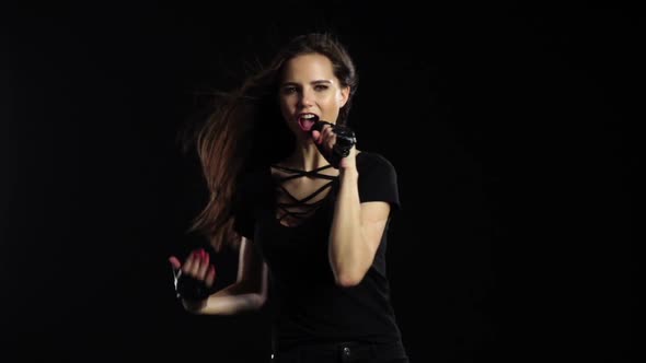 Girl in a Microphone Sings Driving Songs and Smiles. Black Background. Slow Motion alt