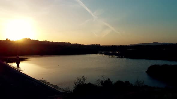 Aerial sunset shot with sun on the horizon towards the left while flying over lake