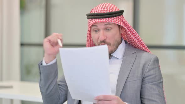 Middle Aged Arab Businessman Celebrating Success while Reading Documents in Office alt