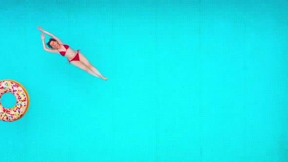 View From the Top As a Woman in a Red Swimsuit Lying on Her Back in the Pool alt