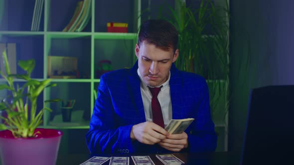Young Businessman Counts Money Putting Them in Piles on Table in Office alt