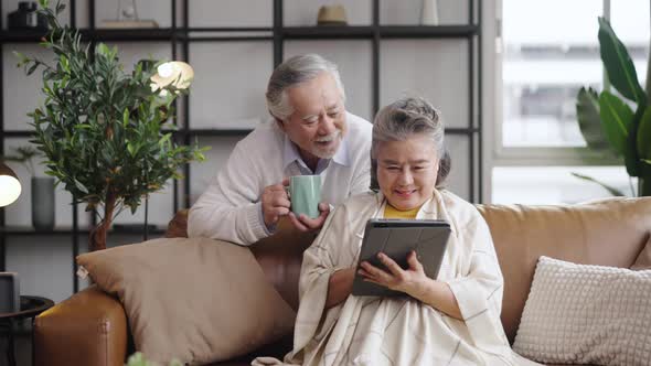 Asian mature senior couple using tablet and spending time together in living room at home.