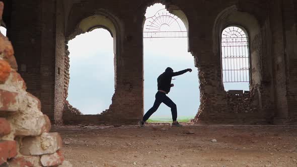 Man boxer in the hood trains beats in an abandoned building. Shadow Boxing. Outdoor workout. alt