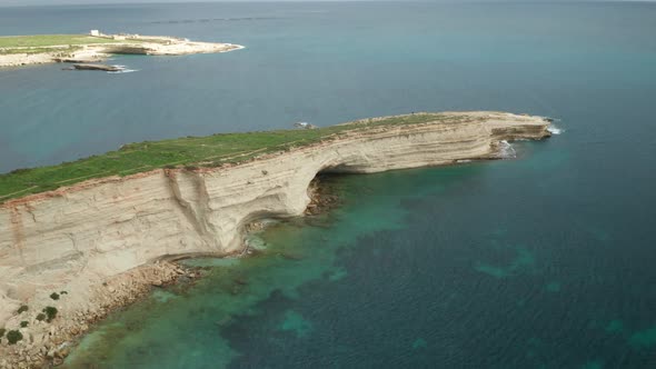 AERIAL: Ras il-Fniek Point in Marsaxlokk with Turquoise Mediterranean Sea Waves Crashing in Shore