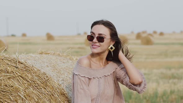 Gorgeous Woman in Sunglasses Caresses Blowing Hair and Naked Shoulder in Field alt