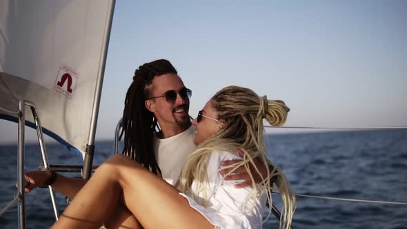 Stylish Couple with Dreadlocks in White Clothes and Sunglasses Sitting Embracing on the Bow of the alt